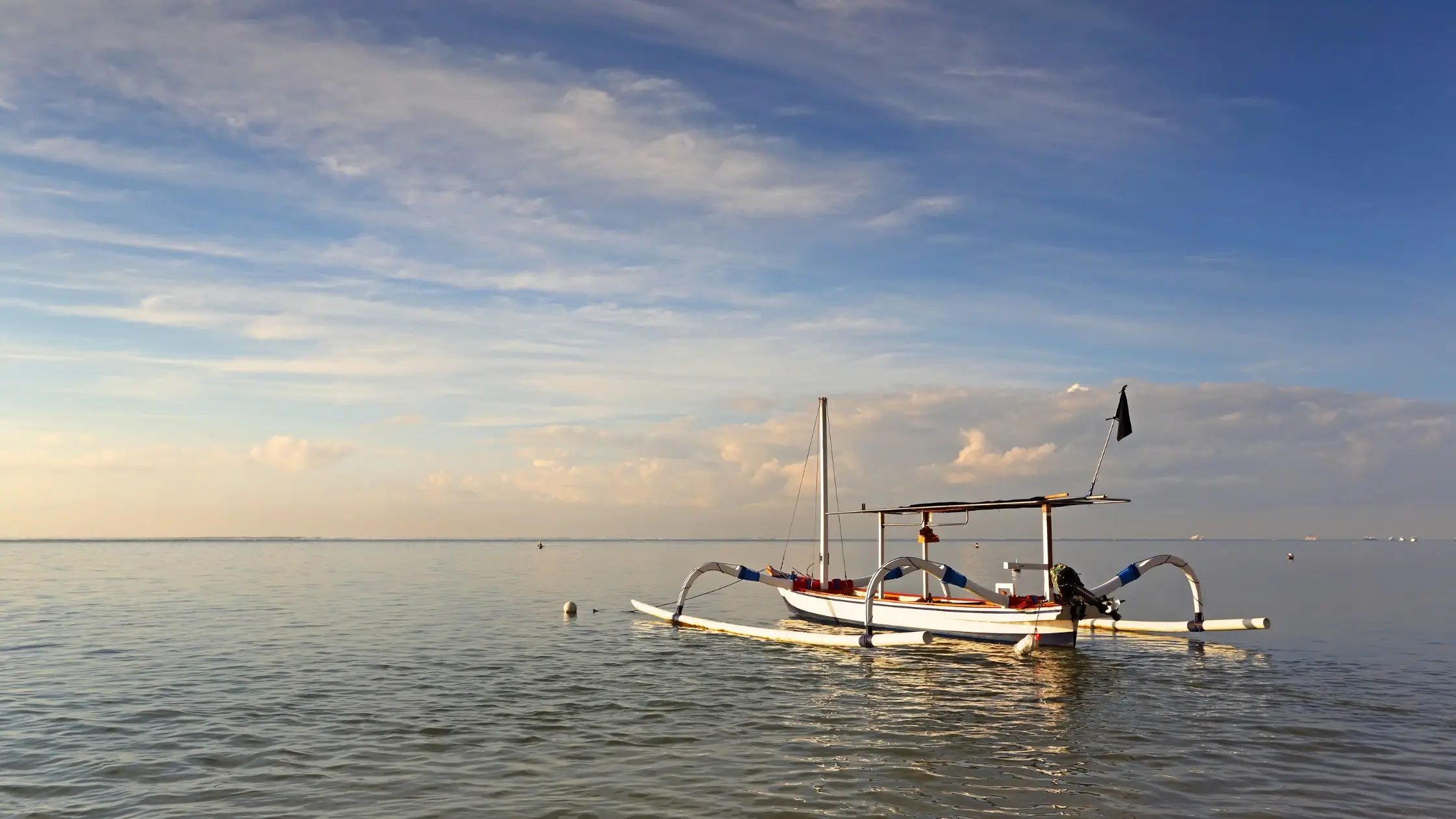 Traditional Balinese jukung boat floating on calm sea at sunset