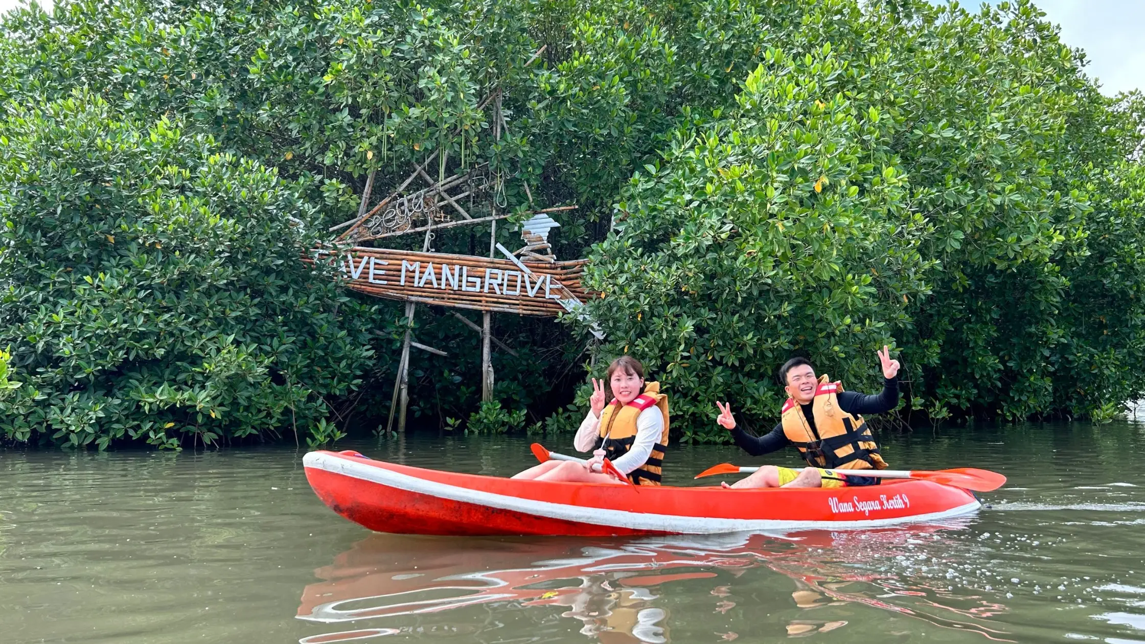 Couple canoeing past ‘Love Mangrove’ sign